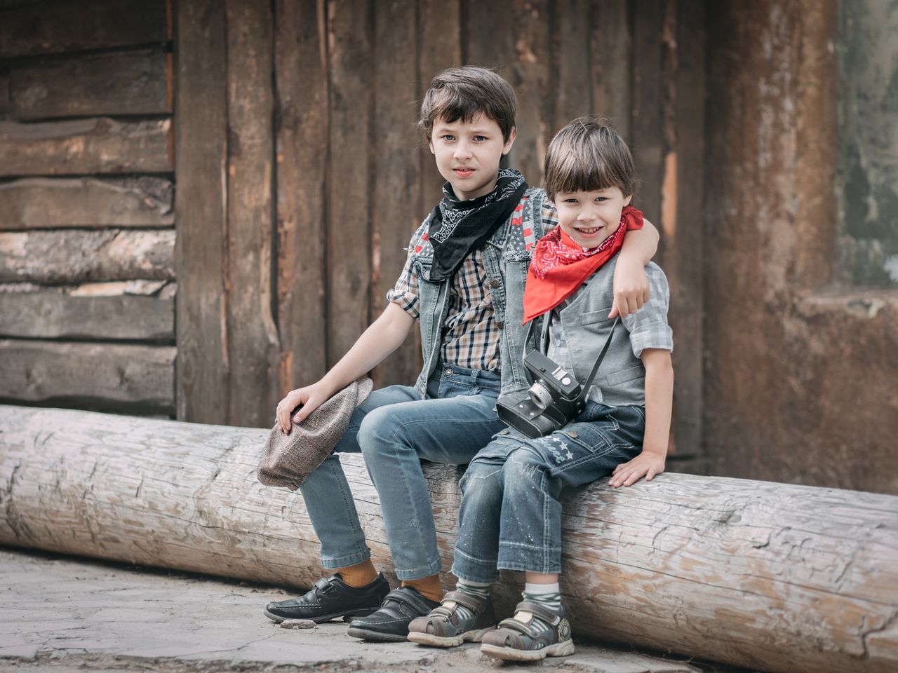 Two boys sitting on a log, cheerful with a vintage camera in hand.